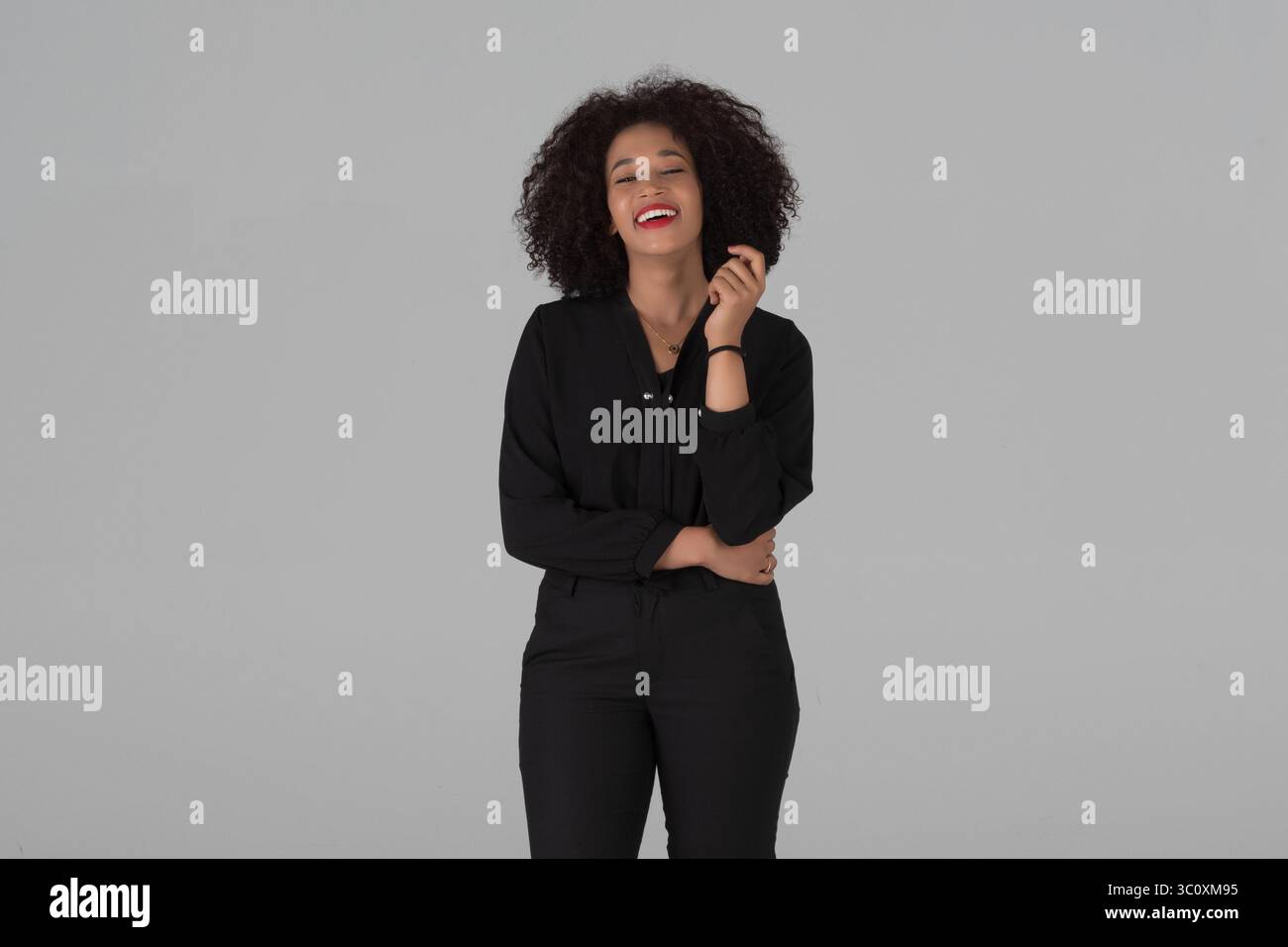 Ein lebhaftes Porträt einer jungen afroamerikanischen Frau mit lockigem Haar, glücklich lachend und ausdrucksvoll echte Freude Studio auf grauem Hintergrund. Stockfoto