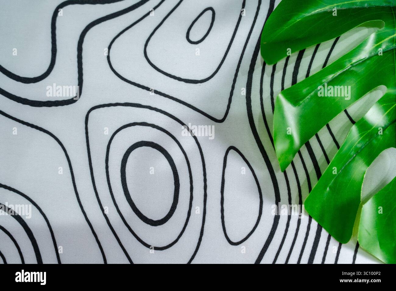 Stoffoberfläche mit abstrakten schwarzen Konturlinien und tropisch grünen Blättern. Perfekt für Hintergrund, Mockups oder modernes visuelles Design mit Natur. Stockfoto