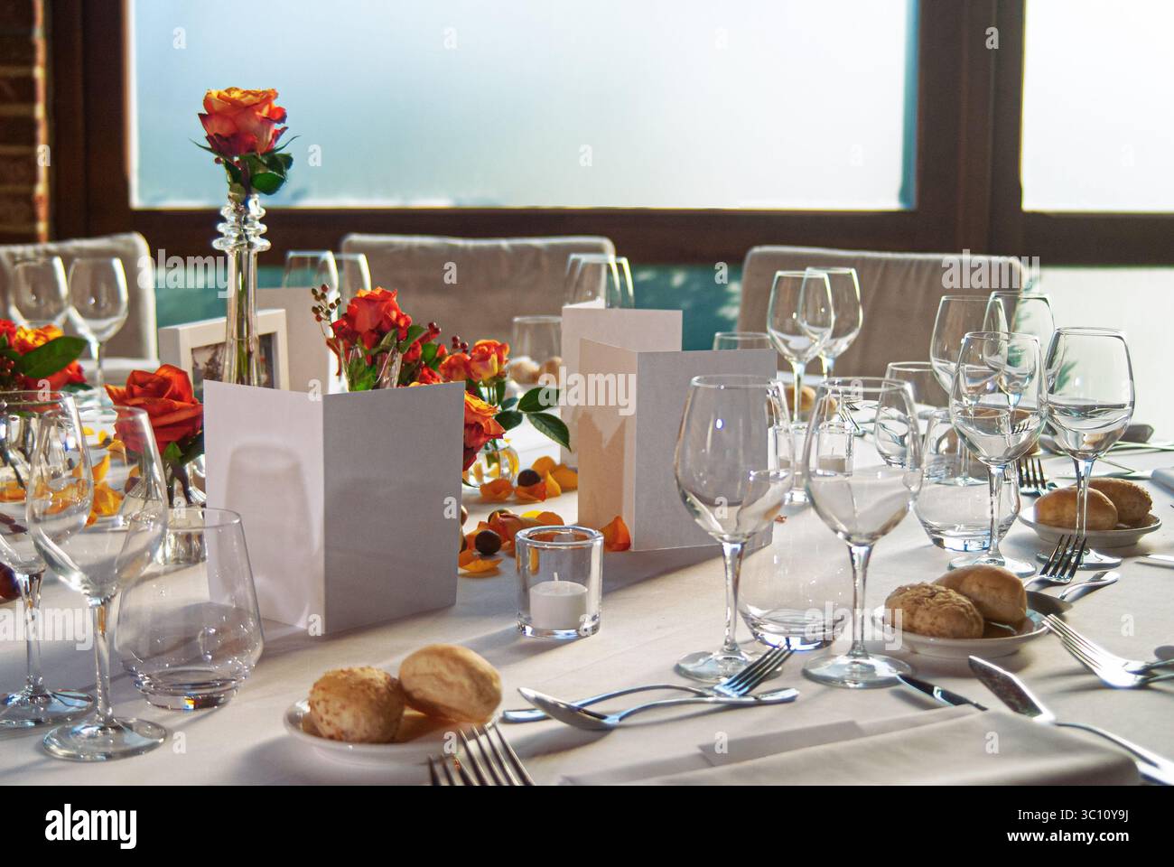 Romantische Szene mit einem dekorierten Esstisch mit Glaswaren, Rosen und Sonnenlicht. Ideal für Feiern, Gelassenheit oder gehobene Restaurants Stockfoto