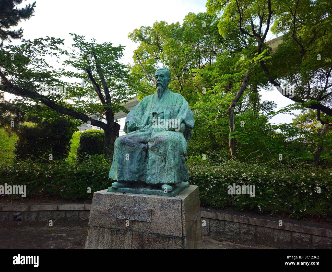 Statue und Denkmal des Sutezo Nishimura, Tenpozan Park Osaka - Gelehrter mit Bronzesitz inmitten grüner Baumkronen Stockfoto