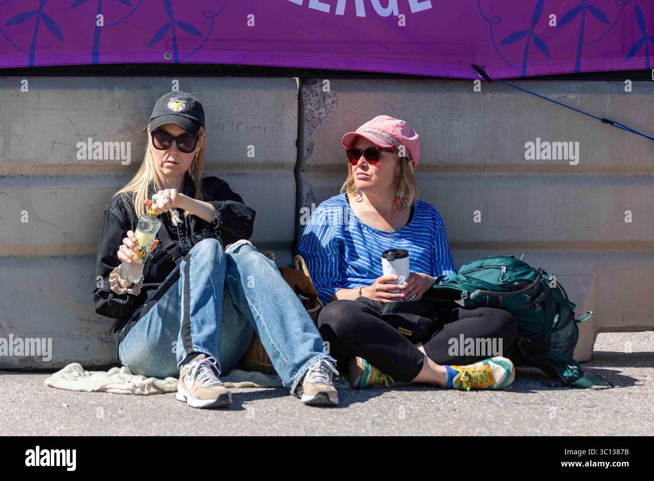 Junge Frauen, die auf dem Boden sitzen und beim World Village Festival im Stadtteil Suvilahti in Helsinki, Finnland, einen Drink trinken Stockfoto