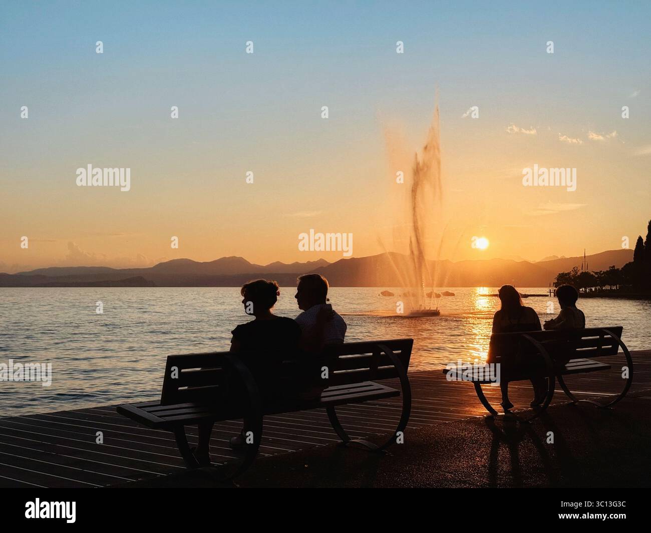 Die Leute sitzen auf Bänken und beobachten den Brunnen am Bardolino See bei Sonnenuntergang. Gardasee, Italien Stockfoto