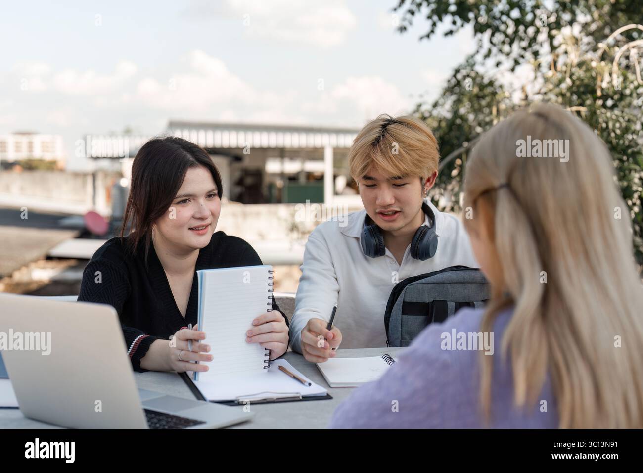 Vielfältige Gruppe junger Studenten, die gemeinsam im Freien mit Laptops und Notebooks in einem modernen Bildungsumfeld arbeiten und studieren Stockfoto