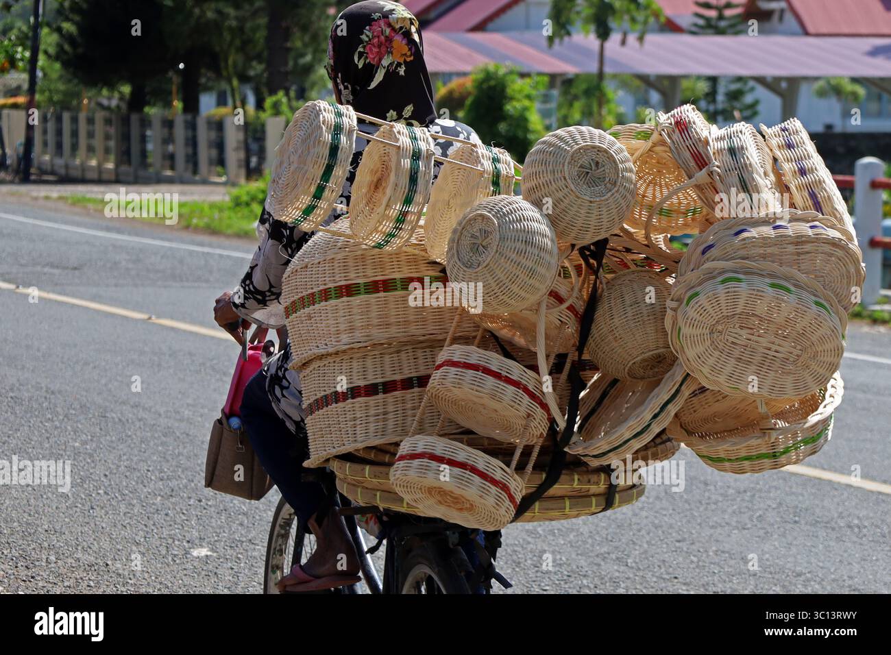 22. Juli 2025, Aceh Besar, Aceh, Indonesien: Eine ältere Frau trägt Handwerksprodukte aus Rattan auf einem Fahrrad in die Innenstadt, während sie an der Lhoknga Road Area im Regency Aceh Besar, Provinz Aceh, Indonesien vorbeifährt. Präsident der Vereinigten Staaten Donald Trump kündigte an, dass er einen Ausfuhrzoll von 19 Prozent auf alle Produkte aus Indonesien, die auf den US-Markt gelangen, einschließlich Rattan, erheben werde. Laut einer Datenveröffentlichung aus dem Jahr 2024 ist Indonesien einer der größten Exporteure von Rattan auf den US-Markt und sogar in die Welt, mit einer Verarbeitungsleistung von 158,5 Millionen US-Dollar Stockfoto