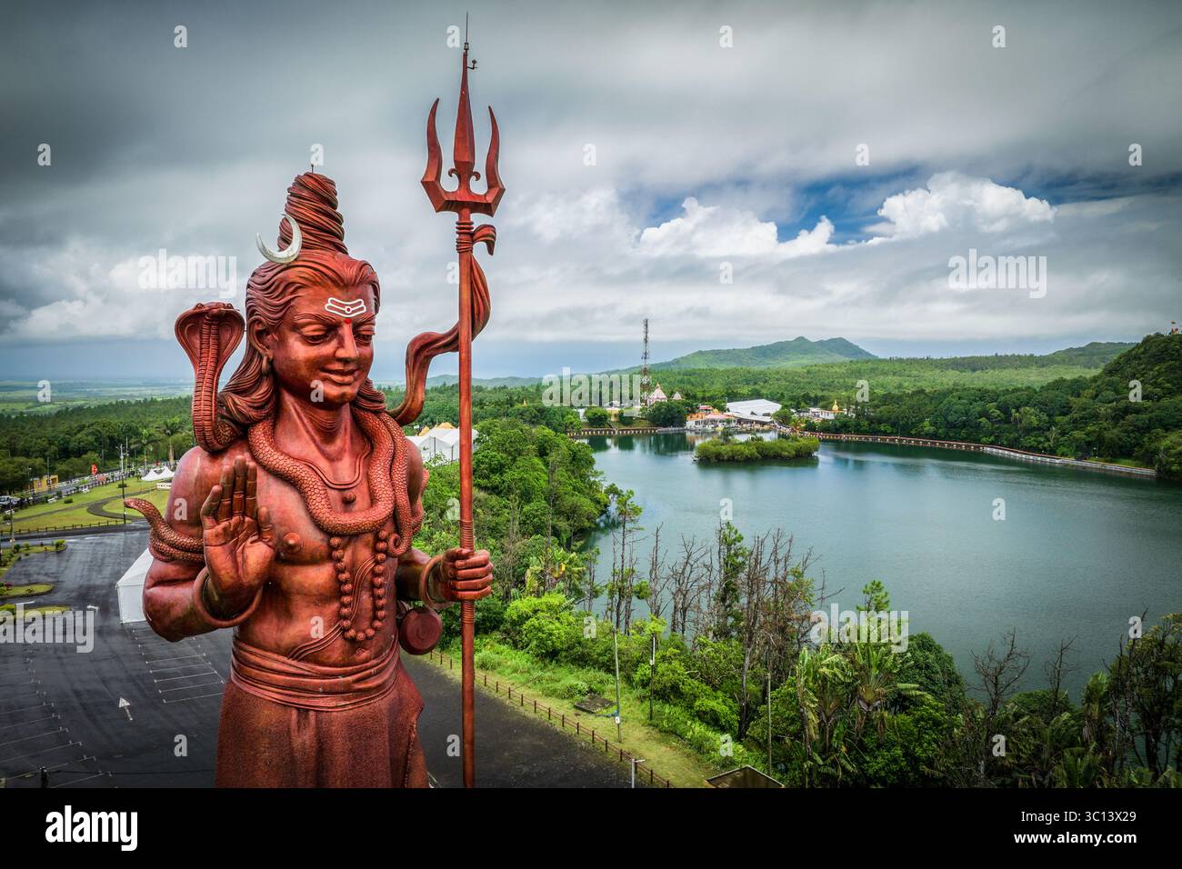 Blick aus der Vogelperspektive auf die majestätische Statue von Lord Shiva, die hoch steht vor dem Hintergrund des ruhigen Ganga Talao Sees und des üppigen Grüns, Grand Bassin, Mauritius. Stockfoto