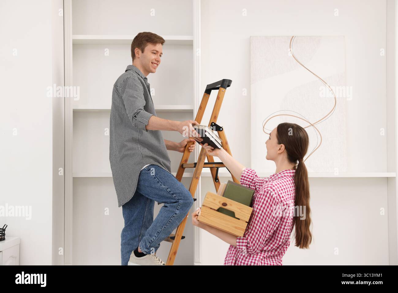 Ein Paar, das Bücher zu Hause mit einer Leiter in die Regale legt Stockfoto