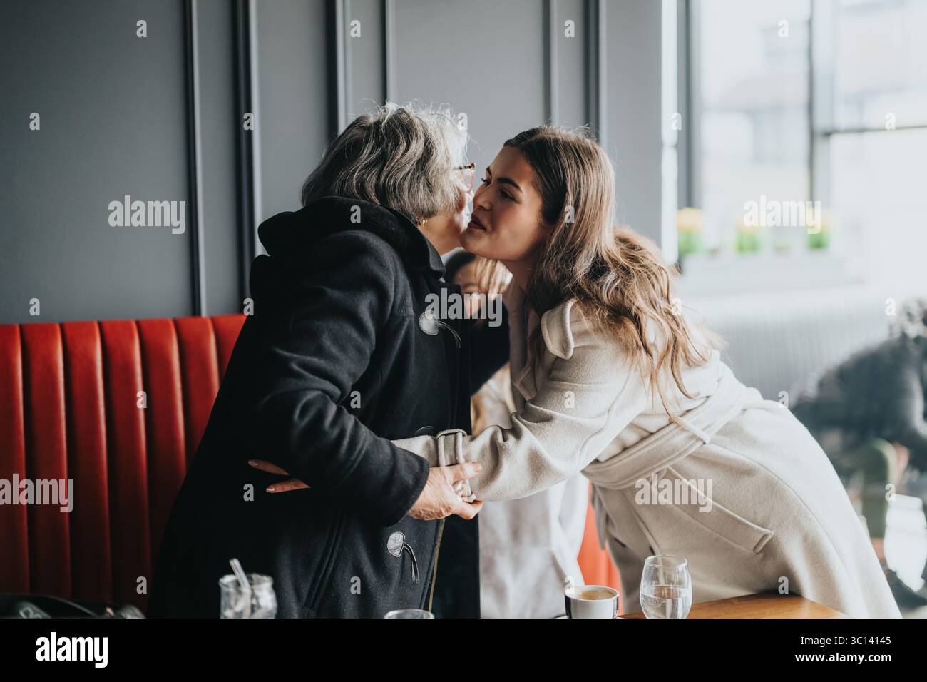 Eine ältere Frau und eine jüngere Frau teilen einen herzlichen Moment in einem gemütlichen Café Stockfoto