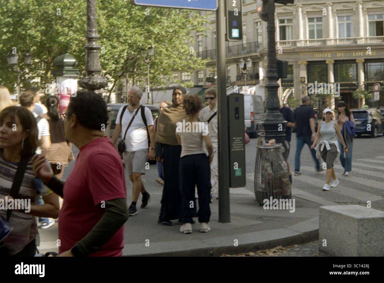 Geschäftige Sommerszene vor dem Hôtel du Louvre, Paris. Verschiedene Fußgänger laufen und interagieren im Nachmittagslicht in der Nähe eines Metroeingangs. Stockfoto