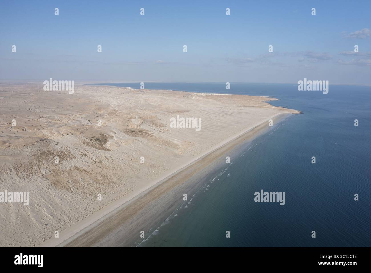 Aus der Vogelperspektive auf den starken Kontrast zwischen der trockenen Wüste und dem tiefblauen Meer, eine faszinierende Küstenlandschaft, Muscat, Muscat Governorate, Oman. Stockfoto