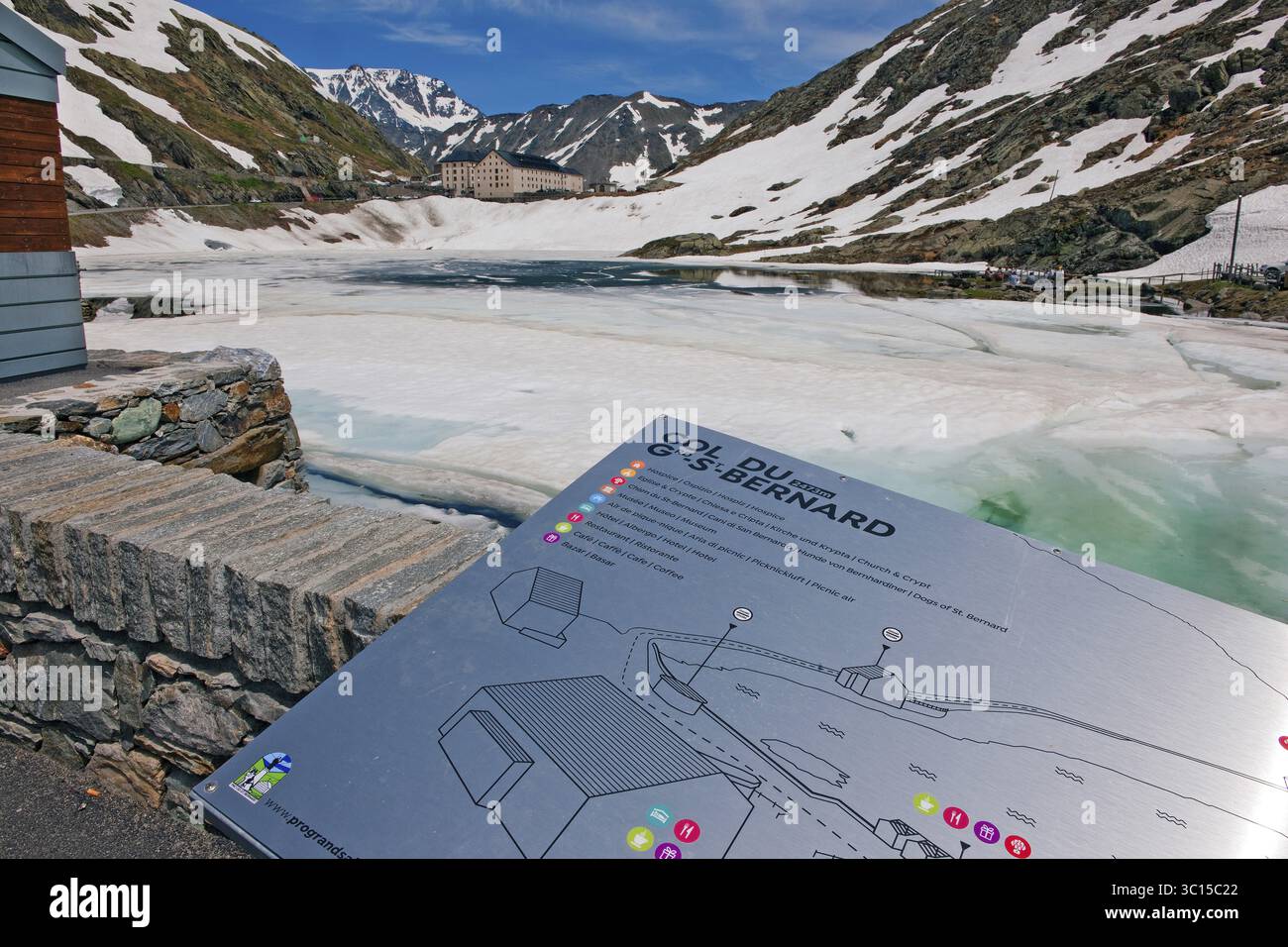 Touristeninformationstafel des Großen Bernhardiner Passes, dahinter Pass Gipfel mit eisigem See Lago di Gran San Bernardo, Wallis, Schweiz, Aostatal Stockfoto
