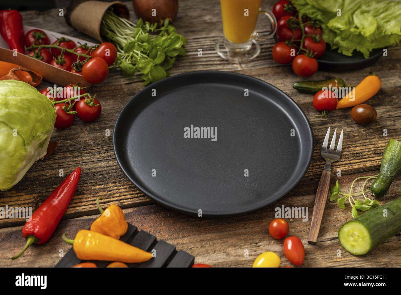 Schwarzer Teller auf Holztisch und -Gabel, Messer mit Holzgriff, viel Gemüse, Draufsicht Stockfoto