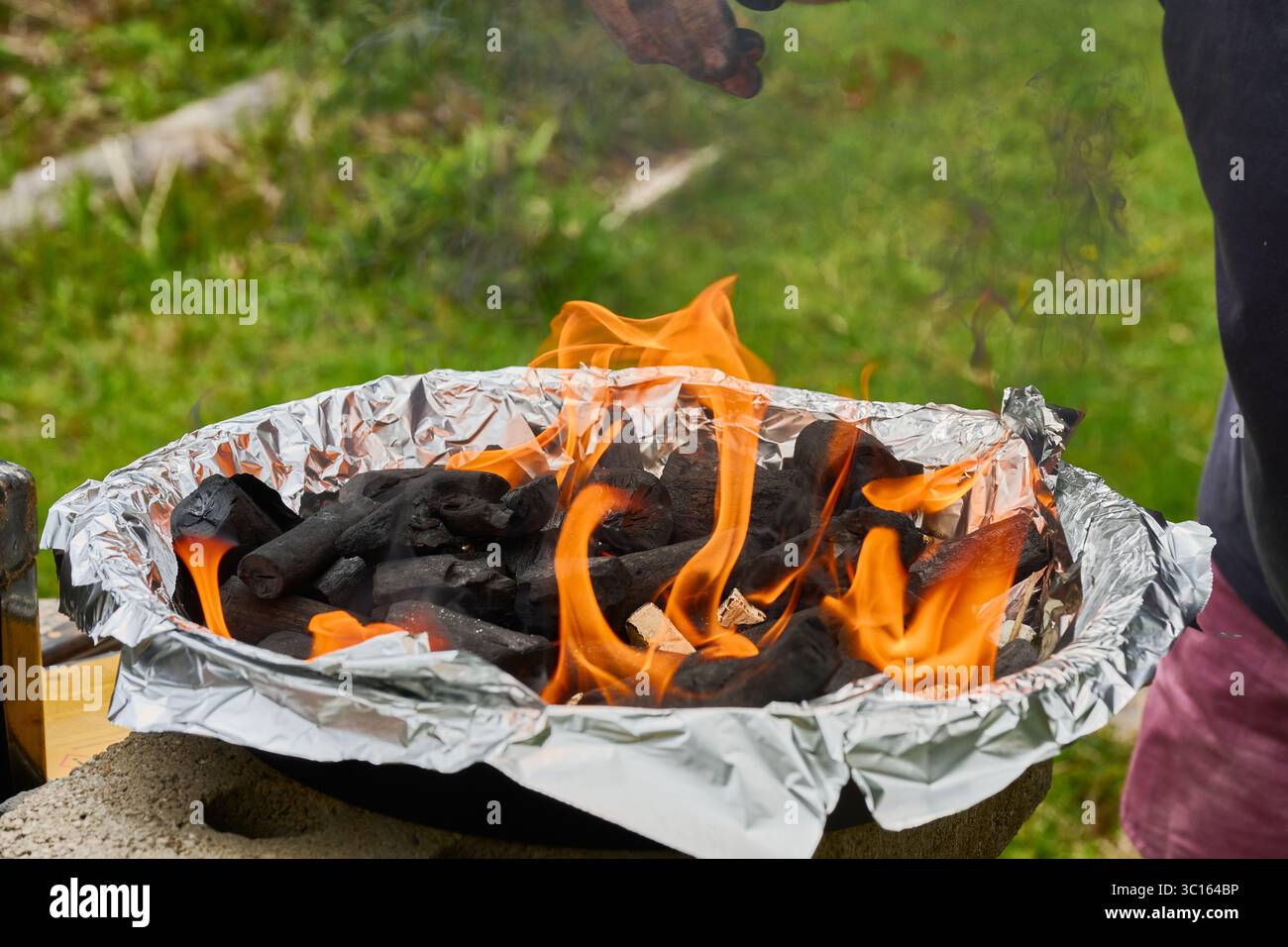 Holzkohle brennt in Flammen in einem tragbaren Grill, der mit Aluminiumfolie bedeckt ist und für das Grillen im Freien bereit ist Stockfoto