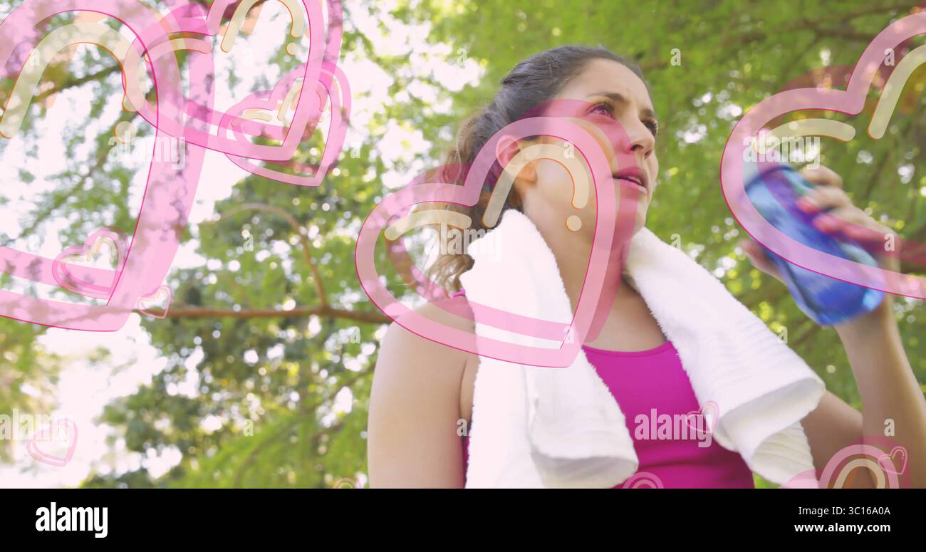 Mit Sportoberteil, Wasserflasche und Handtuch im Park mit rosafarbenen Herzgrafiken, Kopierraum Stockfoto