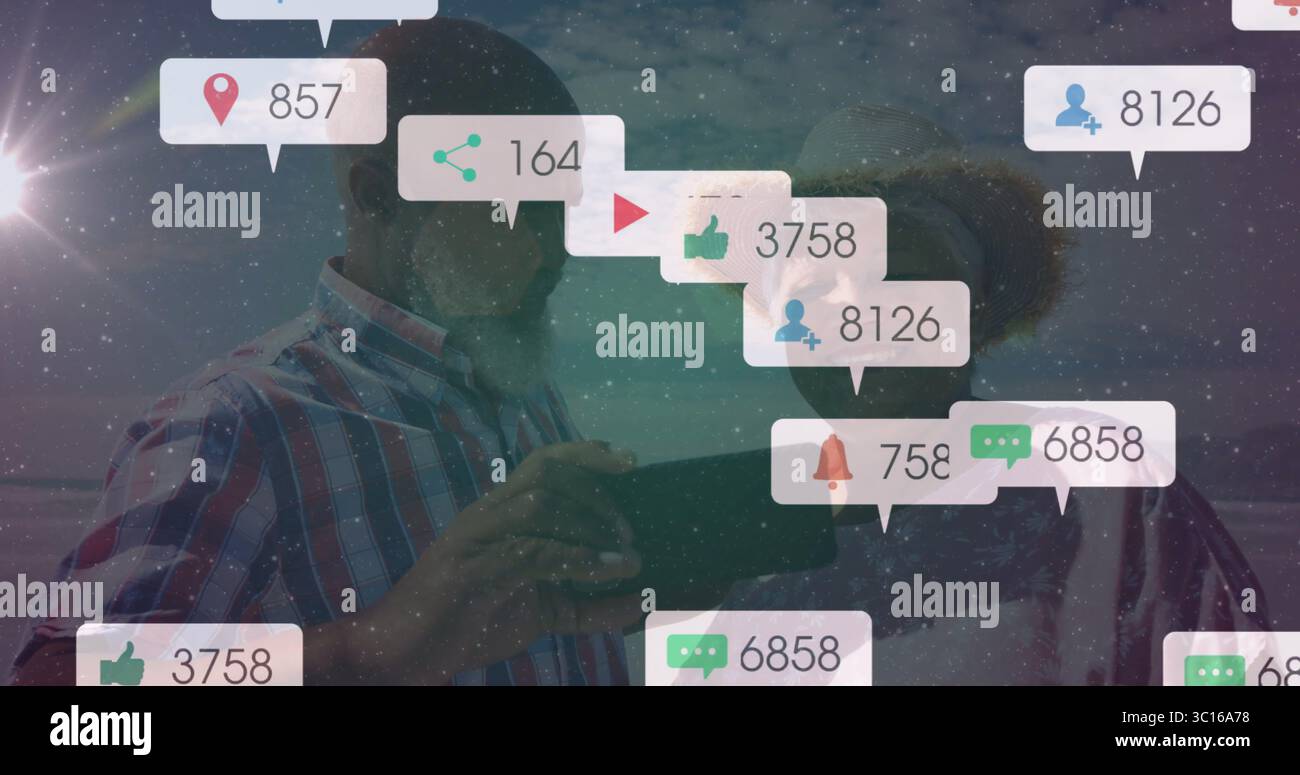 Reifes Paar in kariertem Hemd, Strohhut, Sonnenbrille mit Tablette am Strand, zeigt Benachrichtigungen Stockfoto