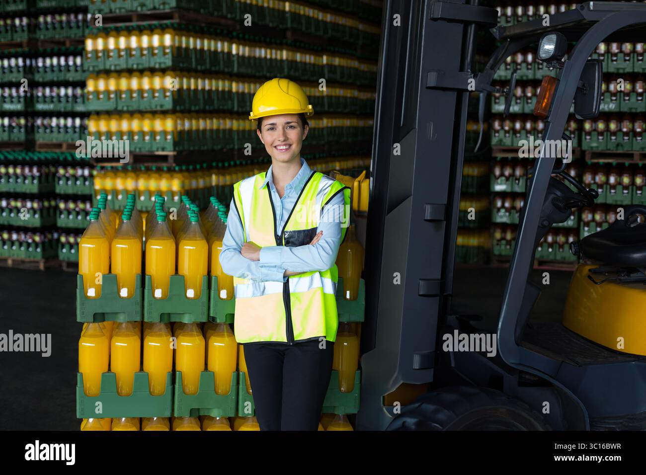 Frau mit Sicherheitsweste und Schutzhelm, die Getränkepaletten im Lager neben dem Gabelstapler inspiziert Stockfoto