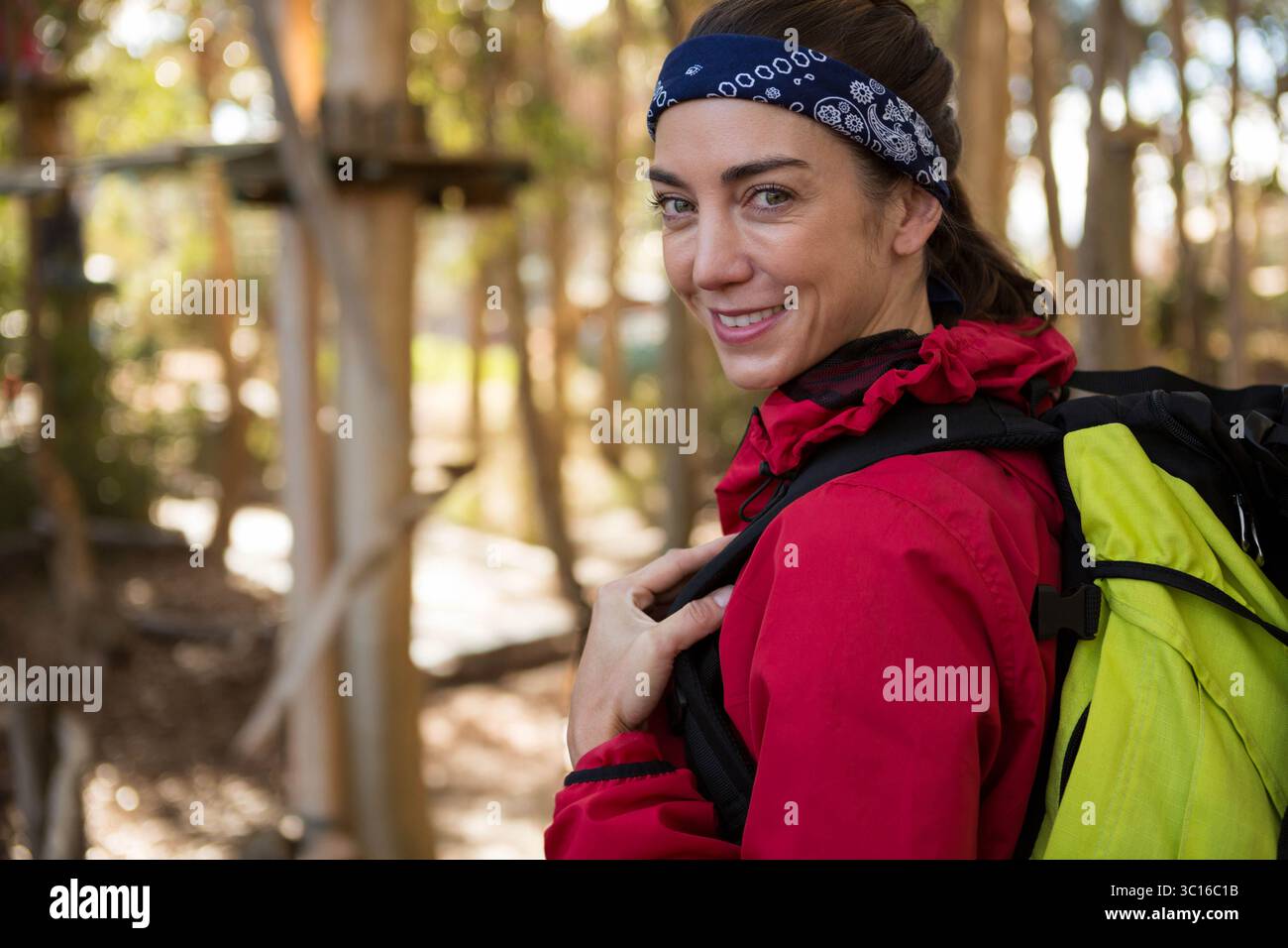 Wanderer, die auf dem Weg steht, trägt rote Jacke, blaues Bandana und trägt grünen Rucksack in der Nähe von Seilen Stockfoto