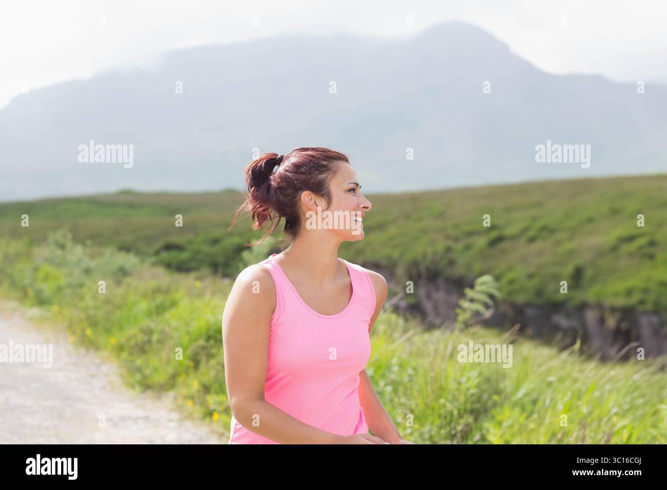 Frau, die auf einem Schotterweg durch grasbewachsene Hügel joggt, mit rosa Tanktop, Kopierraum Stockfoto