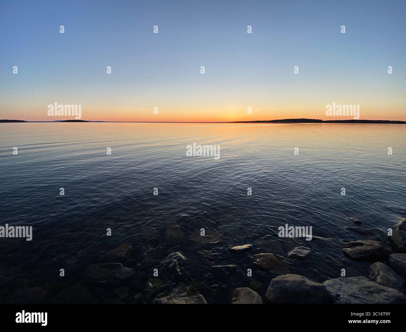 Der Sonnenuntergang färbt den Himmel mit leuchtenden Farben, die sich im stillen Seewasser widerspiegeln. Stockfoto