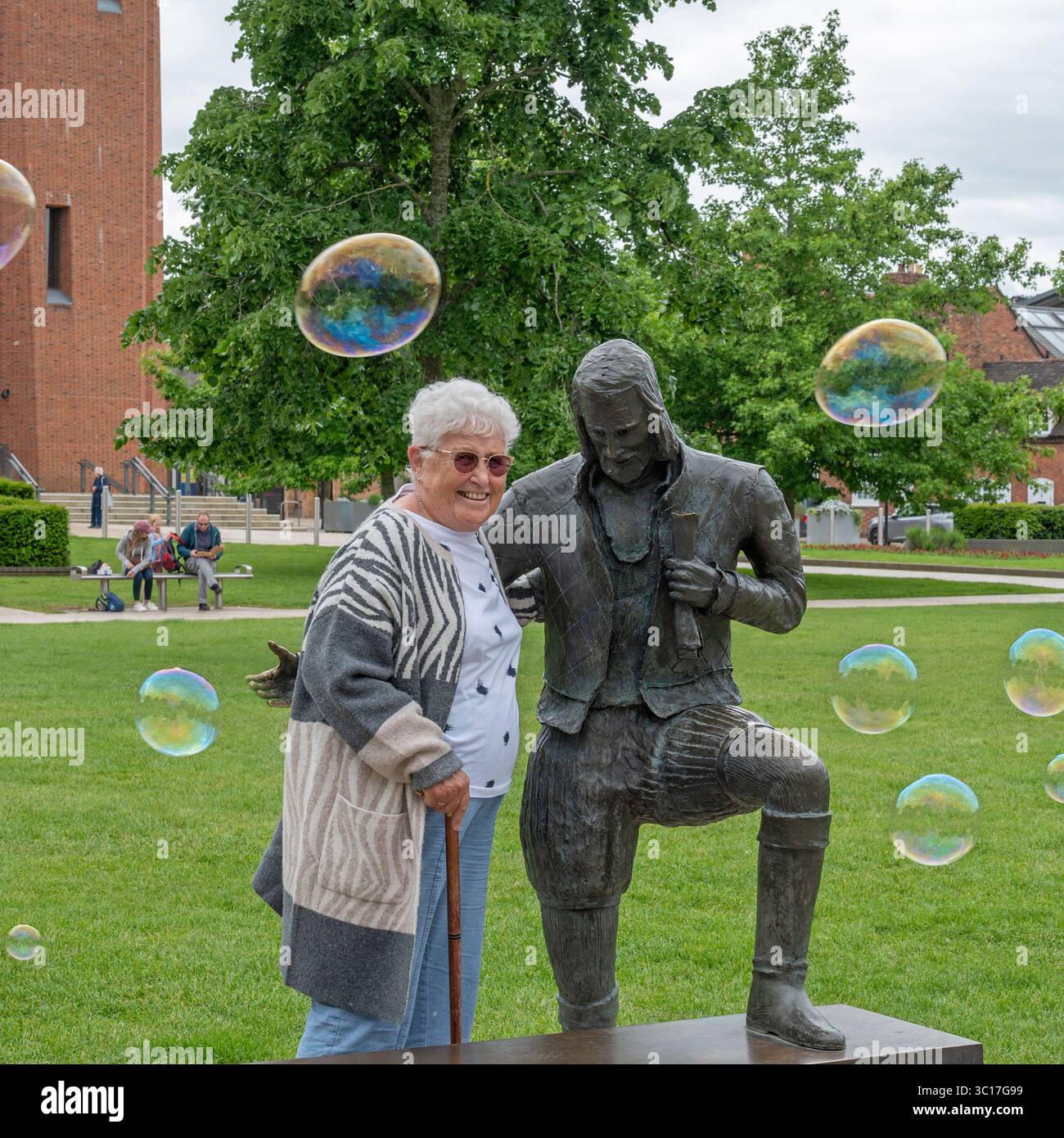 Ein Tourist stand neben einer Skulptur des „Young will“ von Lawrence Holofcener in Bancroft Gardens, Stratford-upon-Avon, Warwickshire, England, UK Stockfoto