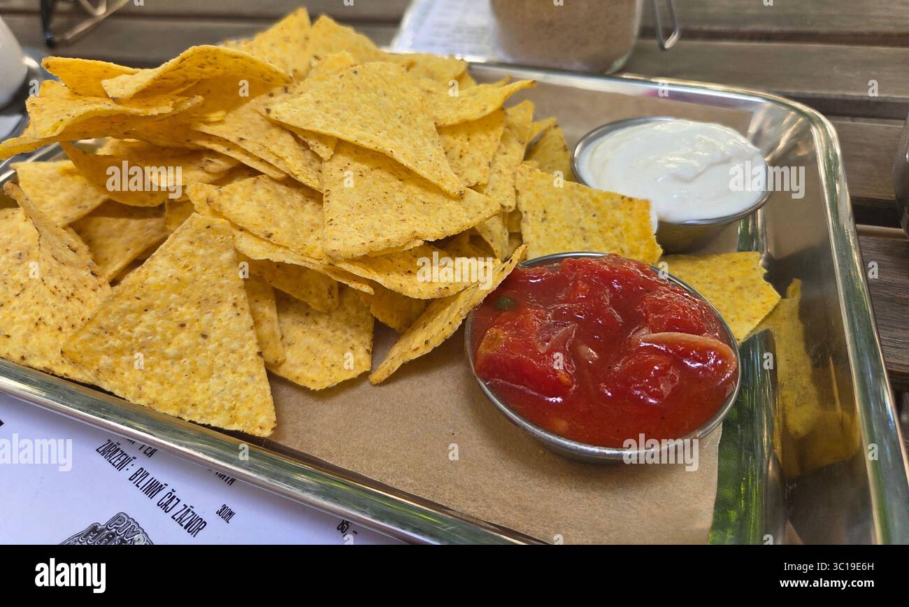 Eine klassische Vorspeise mit knusprigen Tortilla-Chips (Nachos), serviert auf einer Platte mit frischen Tomatensalsa und einem cremigen weißen Dip zum Teilen. Stockfoto