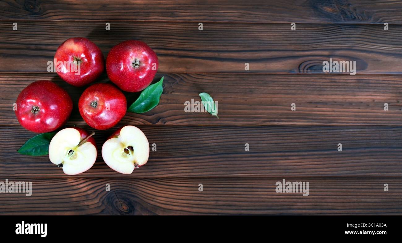 Frische rote Äpfel auf rustikaler Holzoberfläche. Ein Blick von oben auf fünf frische rote Äpfel auf einer rustikalen Holzoberfläche, von denen zwei in Scheiben geschnitten werden, um sie freizulegen Stockfoto
