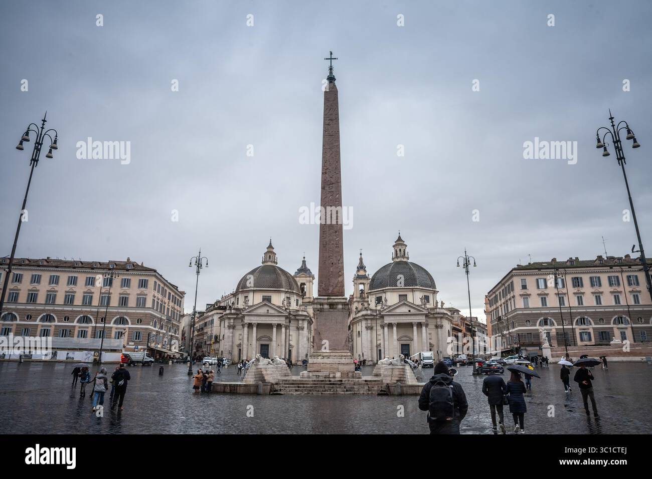 ROM, ITALIEN - 15. JANUAR 2025: Regnerischer Nachmittag auf der Piazza del Popolo in Rom: Der Flaminio Obelisk erhebt sich zwischen zwei Kuppelkirchen, während Menschen mit sich gehen Stockfoto