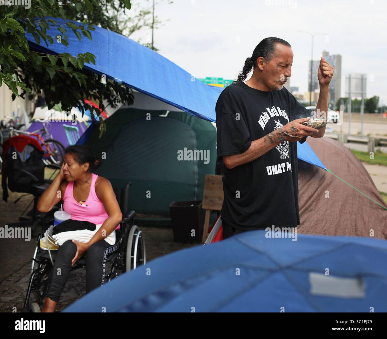 August 2018 – Minneapolis, MN, USA – Yvonne, 32 er sitzt im provisorischen Camp gleich neben Hiawatha und Cedar Avenues, als James Cross, Gründer von Natives Against Heroin, Salbei verbrennt und betet. Später ging er entlang des Lagers, um die Menschen und ihre Zelte in einer Reinigungsaktion am Dienstag, den 7. August 2018, in Minneapolis, MN, zu verwischen. Yvonne sagte, sie sei vor etwa einem Monat ins Lager gezogen, und sagt, sie fühle sich sicher im Lager, weil sie von Menschen umgeben ist, die sie kennt. „Es ist eine Stärke in Zahlen“, sagte Yvonne, der nach einem Angriff vor einigen Jahren im Rollstuhl sitzt. „Es gibt viele Augen Stockfoto