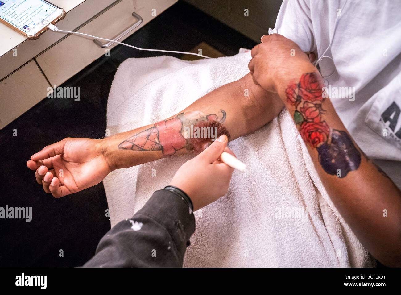 2. Oktober 2018 – Minneapolis, Minnesota, USA – die Assistentin des Kindertheaters Mary Caper trug temporäre Tattoos an den Unterarmen des Schauspielers Dwight Leslie an, um seine Rolle in der „Last Stop on Market Street“ vorzubereiten. Dienstag, 2. Oktober 2018... Tattoos tauchen im echten Leben und auf der Bühne auf, einschließlich aktueller Guthrie- und CTC-Produktionen. Wie kriegen Sie sie an? Wie bekommen Sie sie ab (besonders, wenn Sie nicht wirklich einen Kaffee mit einem Hakenkreuz am Körper trinken wollen, was mit MN Opera ''Dead man Walking'' passiert ist)? Schauspieler Dwight Leslie wird sich vorübergehend Tattoos machen Stockfoto