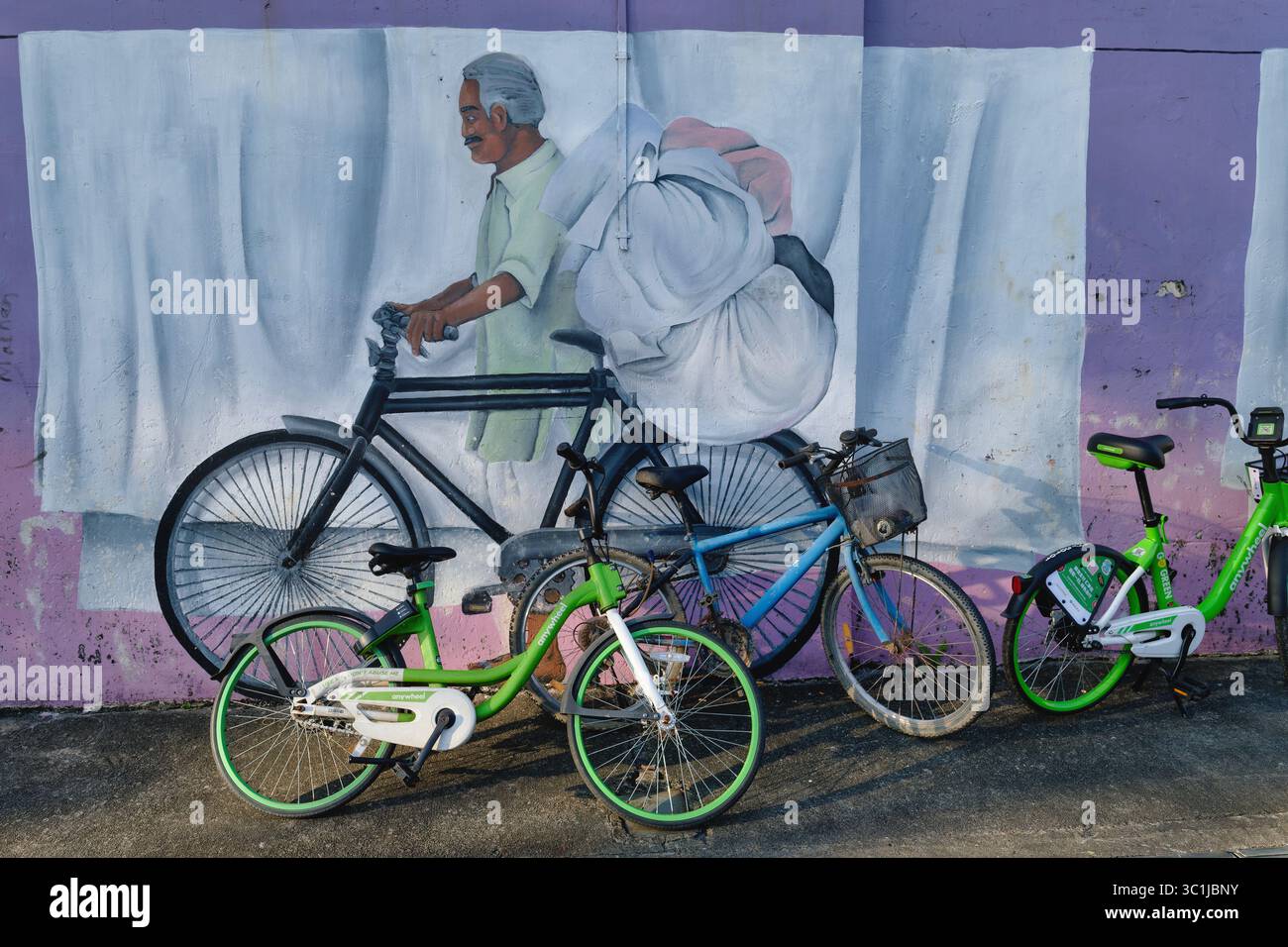Detail eines Wandgemäldes in Little India, Singapur, das einen indischen Dhobi (Waschmann) darstellt, der Wäsche auf seinem Fahrrad transportiert, echte Leihräder in f/g Stockfoto