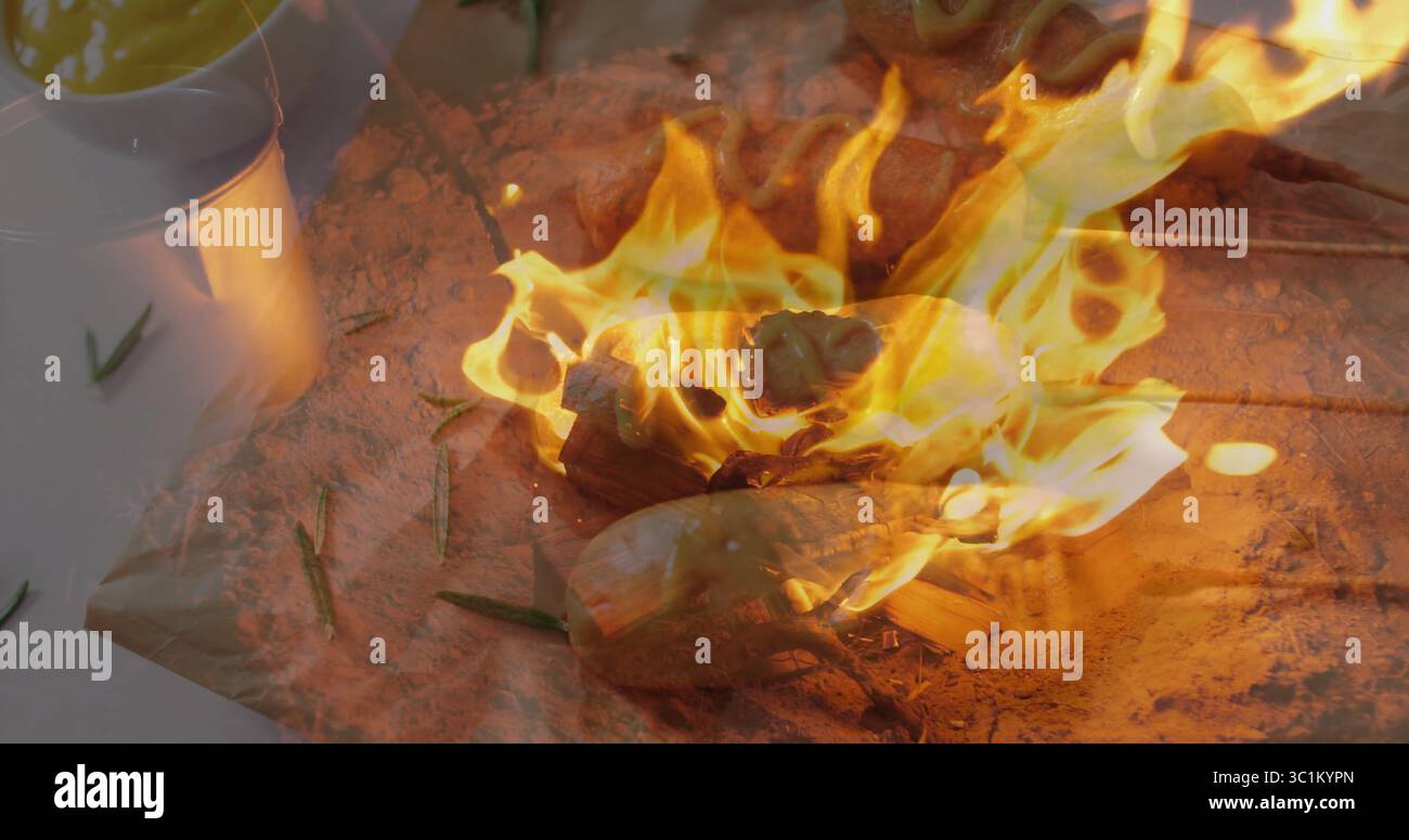 Auf dem Campingplatz im Freien wird Mais auf einer Holzkolbe über offenen Flammen mit Rosmarinzweigen und glühender Glut geröstet Stockfoto Auf dem Campingplatz im Freien wird Mais auf einer Holzkolbe über offenen Flammen mit Rosmarinzweigen und glühender Glut geröstet Stockfoto