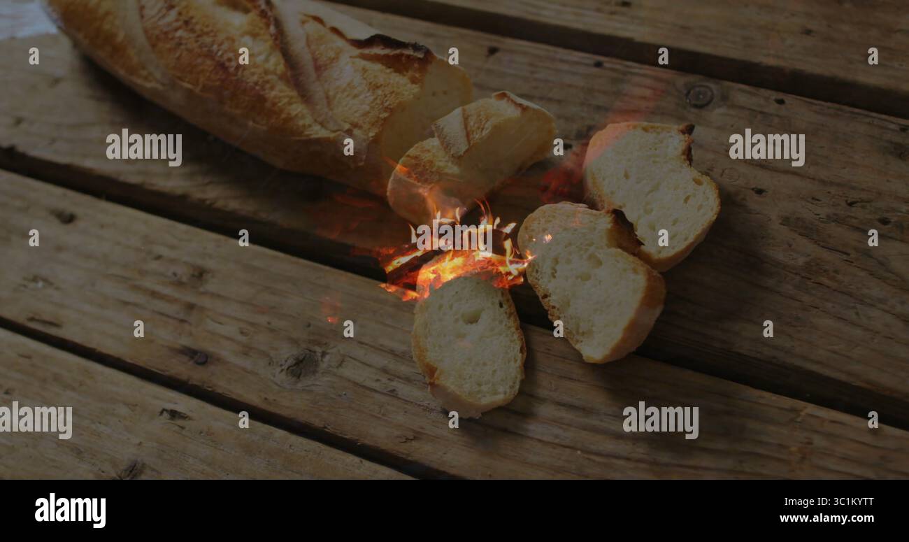 Knisterndes Baguette-Brot auf rustikaler Holzplatte, mit geschnittenen Stücken und Flammen Stockfoto