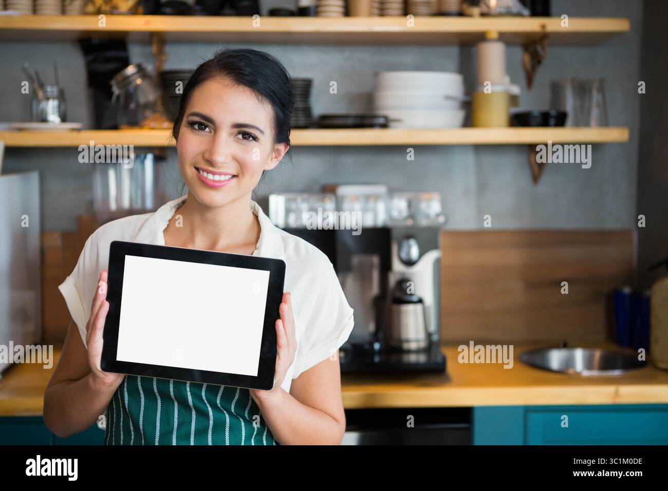 Asiatischer Barista in der Hand eines Tablets mit leerem Bildschirm in der Kaffeeküche neben Espresso-Maschine und Regalen Stockfoto