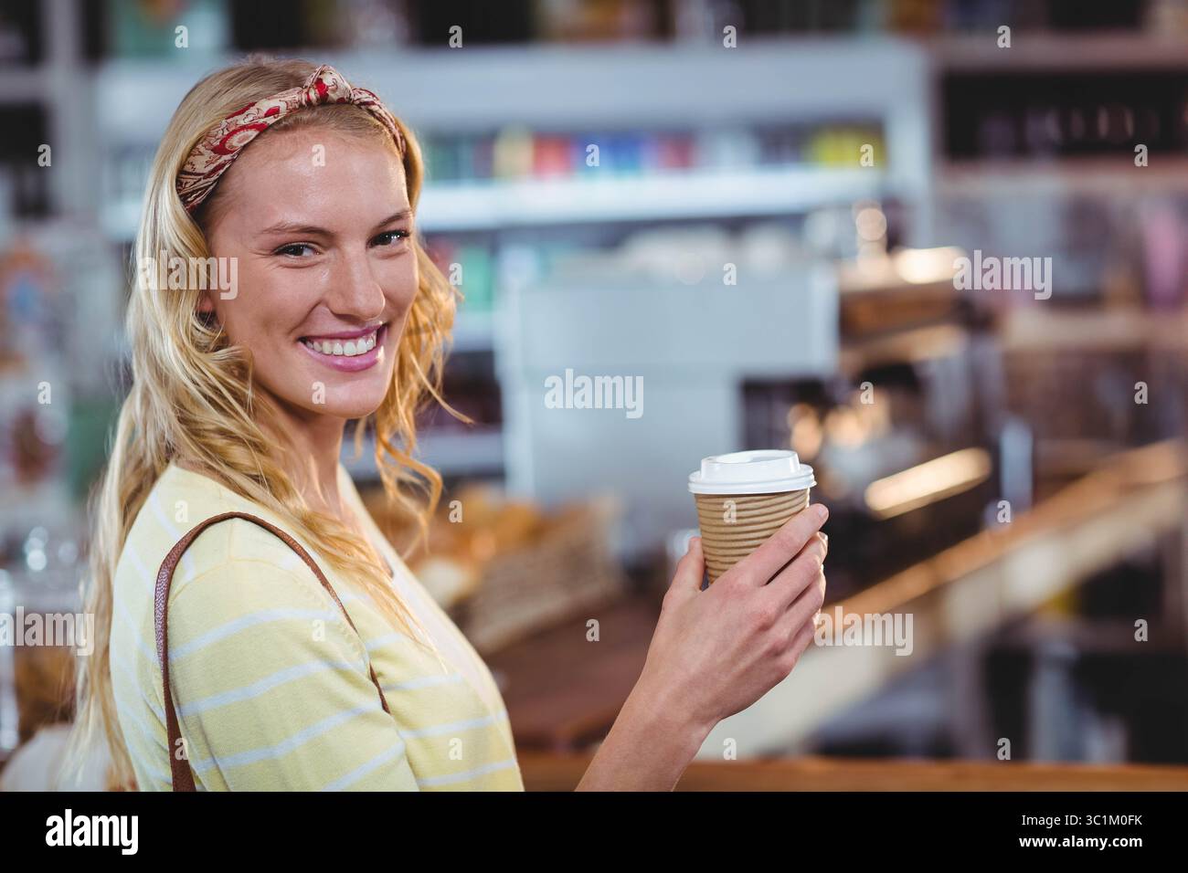 Frau lächelte und hielt eine Kaffeetasse aus geripptem Papier am Kaffeekocher mit Espresso-Maschine und Kopierraum Stockfoto