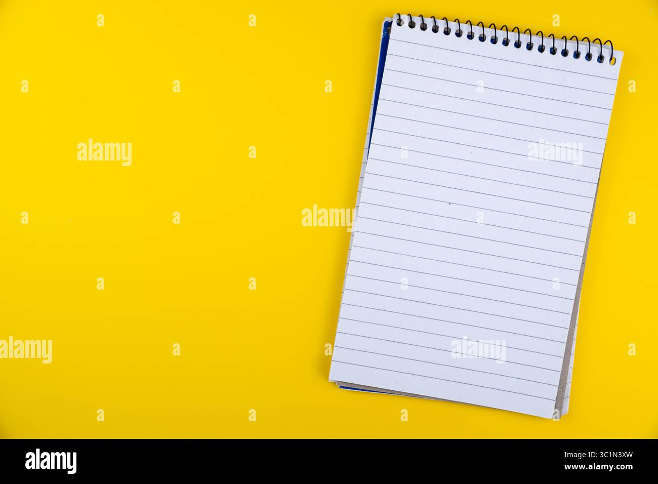 Leeres spiralgebundenes Notizbuch mit linierten Seiten auf leuchtendem gelbem Hintergrund für Notizen und Skizzieranwendungen Stockfoto