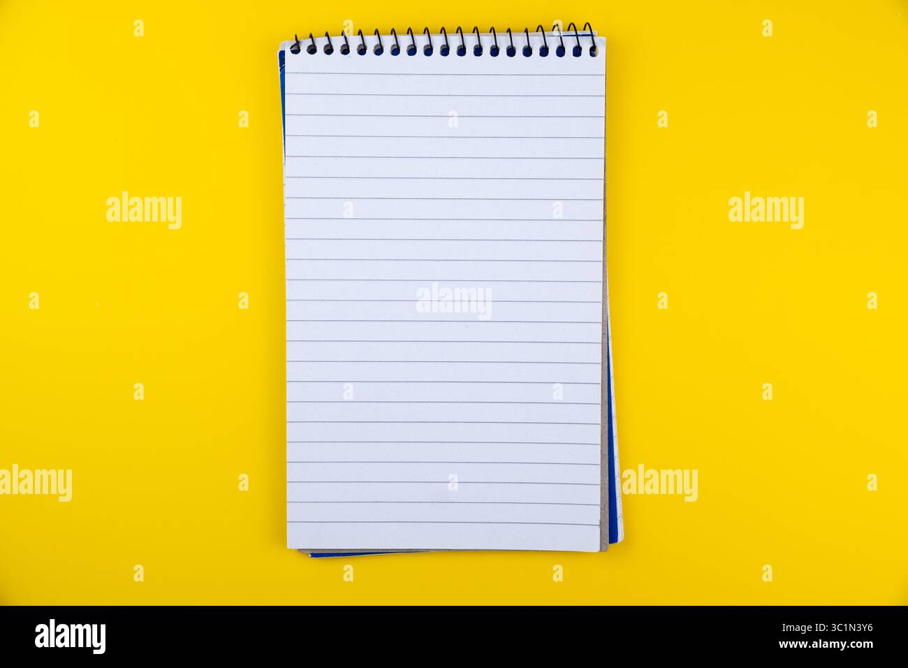 Leeres spiralgebundenes Notizbuch mit linierten Seiten auf leuchtendem gelbem Hintergrund für Notizen und Skizzieranwendungen Stockfoto