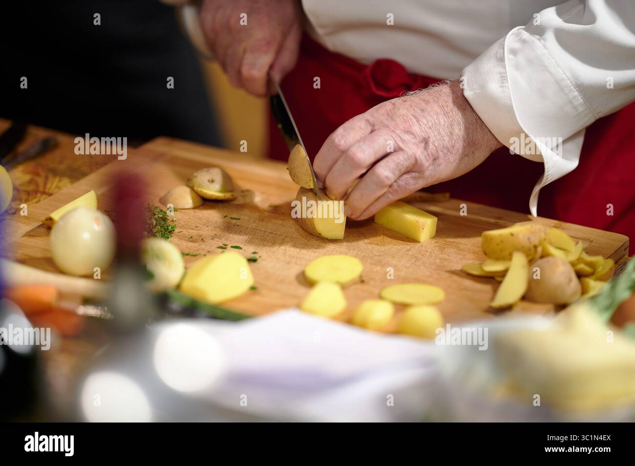 Chefkoch schneidet frische Kartoffeln auf hölzernem Schneidebrett Stockfoto