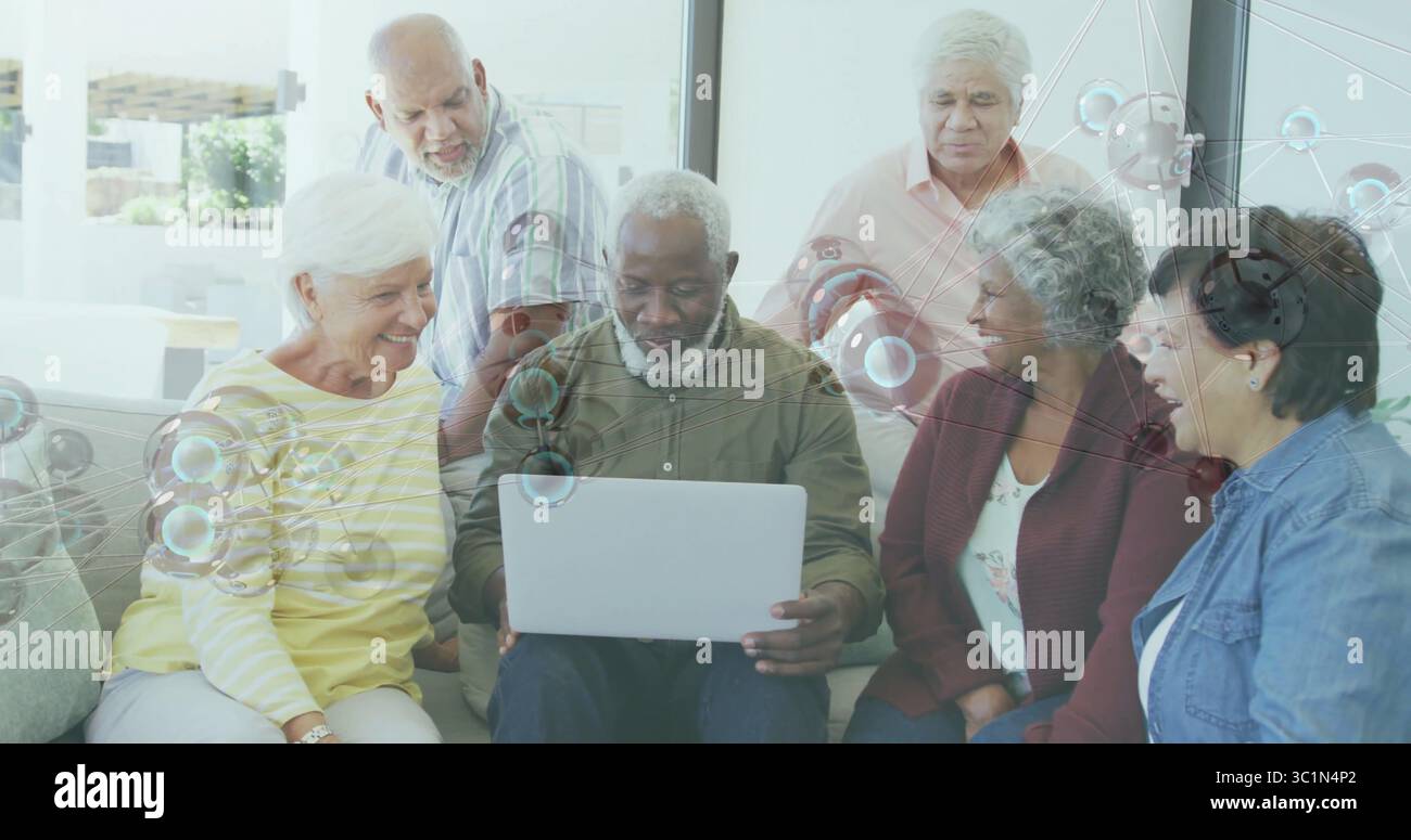Senioren in lässiger Kleidung treffen, die sich um einen silbernen Laptop in der Wohnlounge zusammensetzen Stockfoto