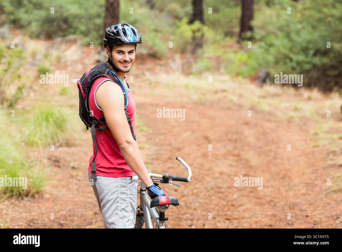 Männlicher Radfahrer mit Mountainbike auf bewaldetem Trail mit Helm und Trinkbeutel, Kopierraum Stockfoto