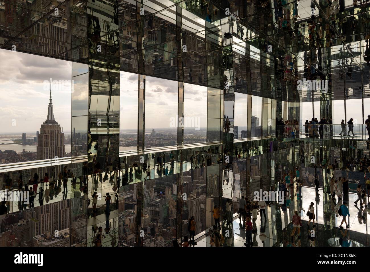 New York, Vereinigte Staaten - 07. Juni 2024: Blick auf das Empire State Building, umrahmt von Spiegeltafeln, die Menschenmassen und das Stadtbild in einer schillernden Licht- und Perspektivendarstellung reflektieren. Stockfoto