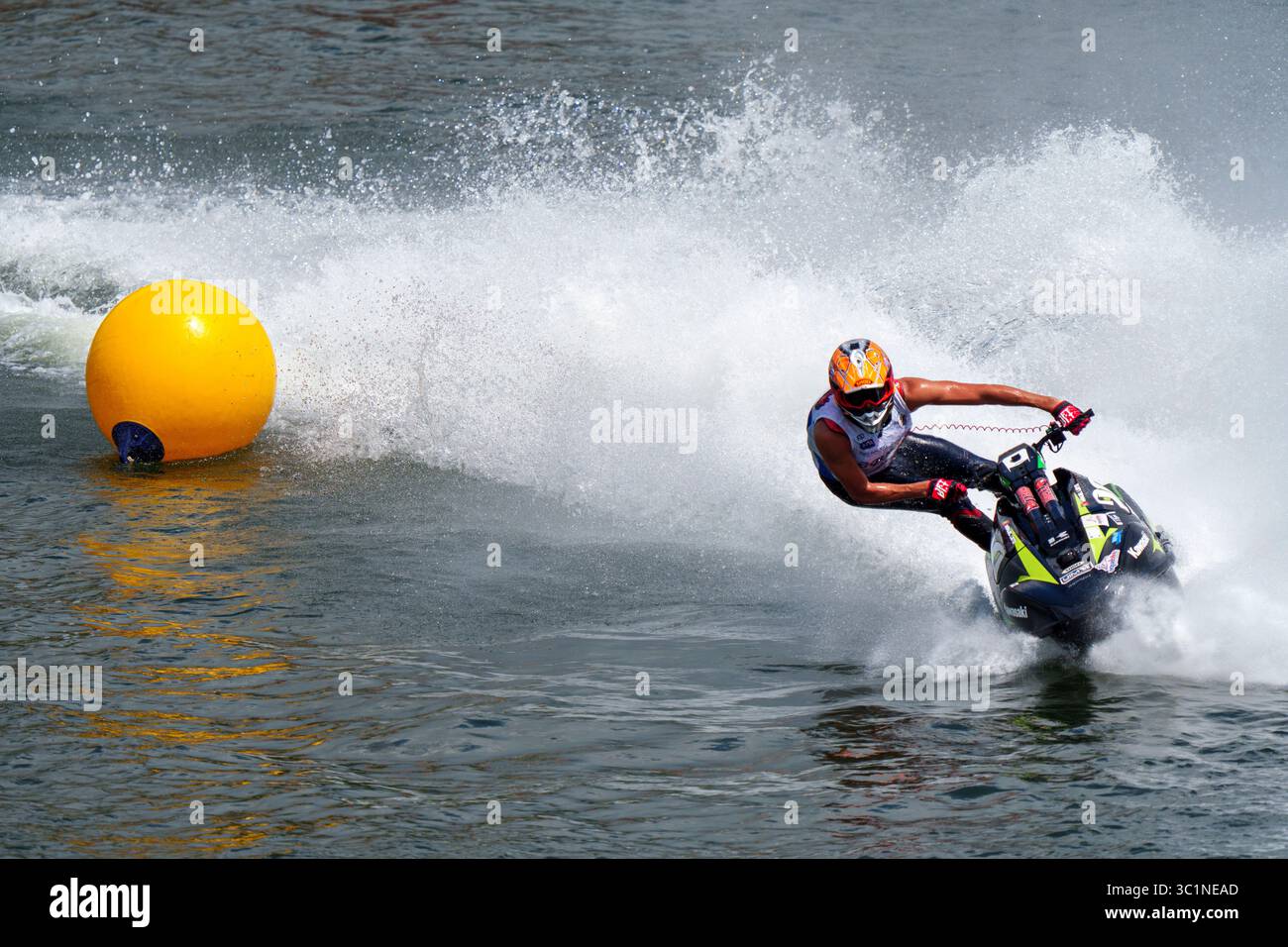 Eine Person, die einen Helm und Rennausrüstung trägt, manövriert einen Jet-Ski geschickt um eine gelbe Boje während eines Hochgeschwindigkeitswasserrennens Stockfoto