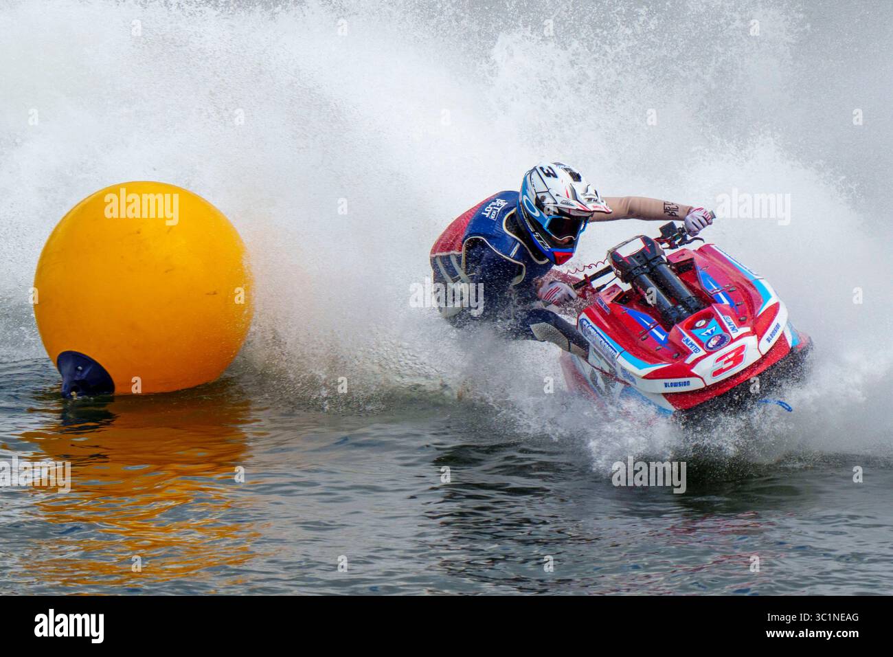 Eine Person, die einen Helm und Rennausrüstung trägt, manövriert einen Jet-Ski geschickt um eine gelbe Boje während eines Hochgeschwindigkeitswasserrennens Stockfoto