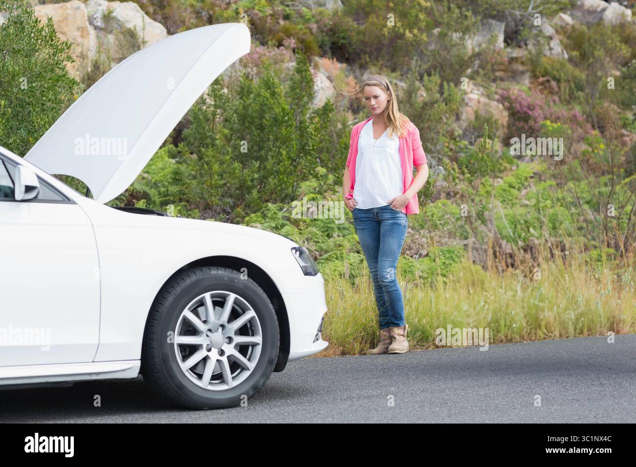 Frau, die auf der Landstraße neben der weißen Limousine steht und die Motorhaube offen hat, untersucht den Motorraum Stockfoto
