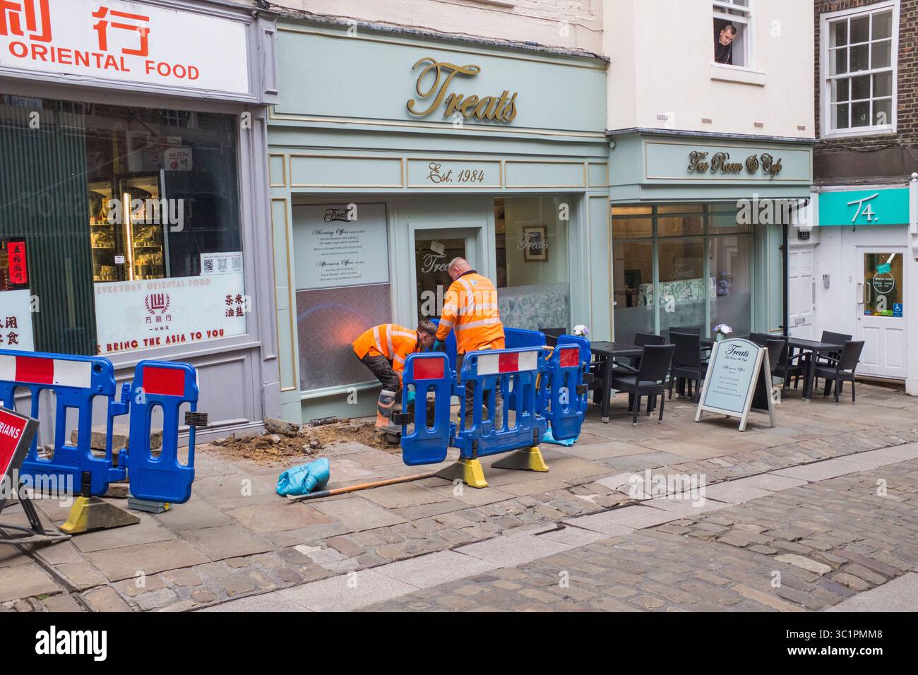 Arbeiter reparieren den Straßenbereich in Silver Street, Durham, England, Großbritannien. Tragen Sie orangefarbene Jacken und verwenden Sie Sicherheitsbarrieren. Stockfoto