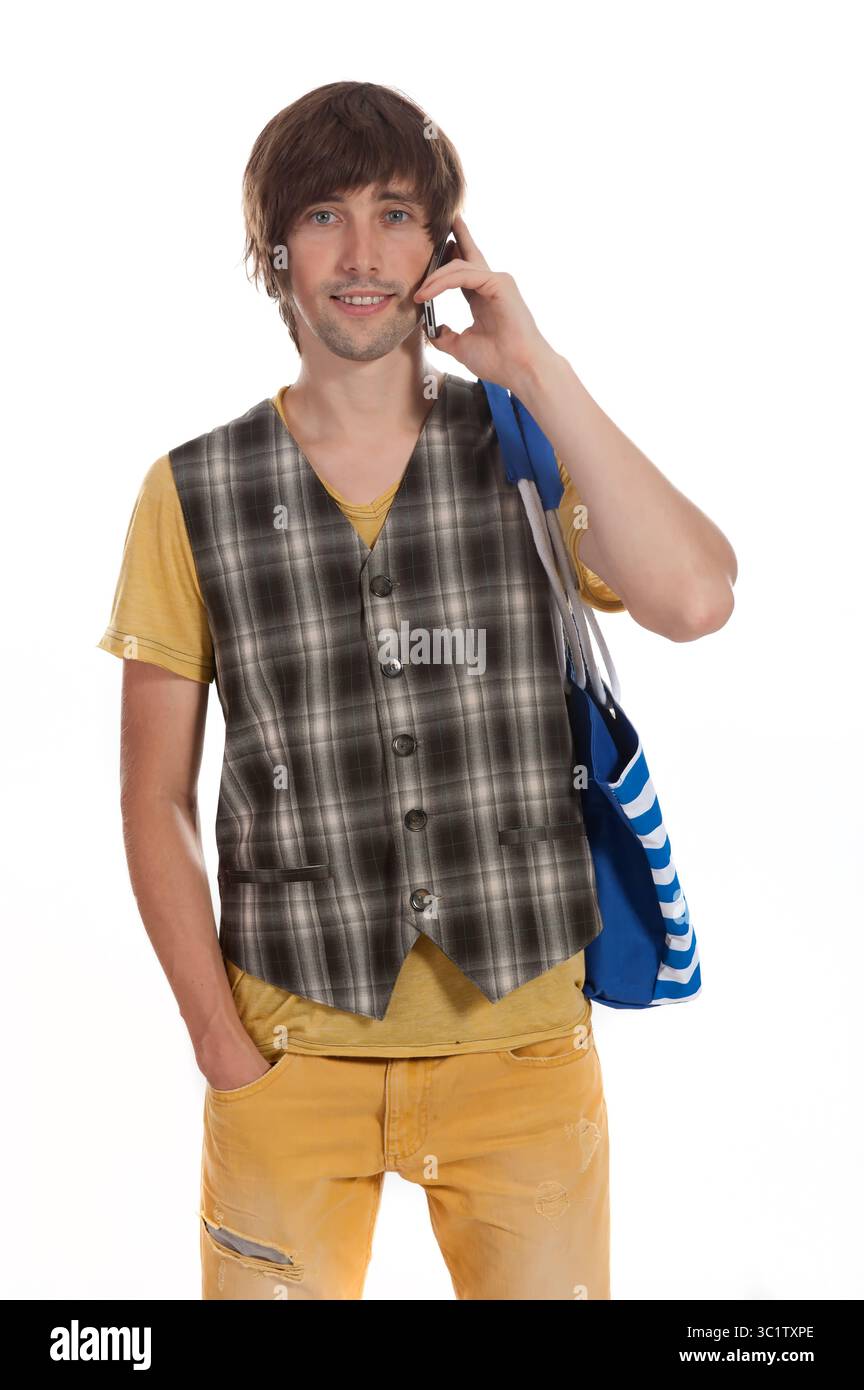 Fröhlicher junger Mann steht beiläufig und spricht mit einer Tragetasche am Telefon. Stockfoto