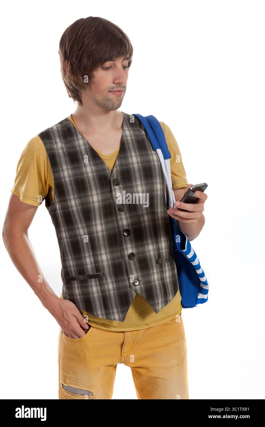Ein lässig gekleideter junger Mann steht mit einem Telefon in der Hand, konzentriert und entspannt. Stockfoto