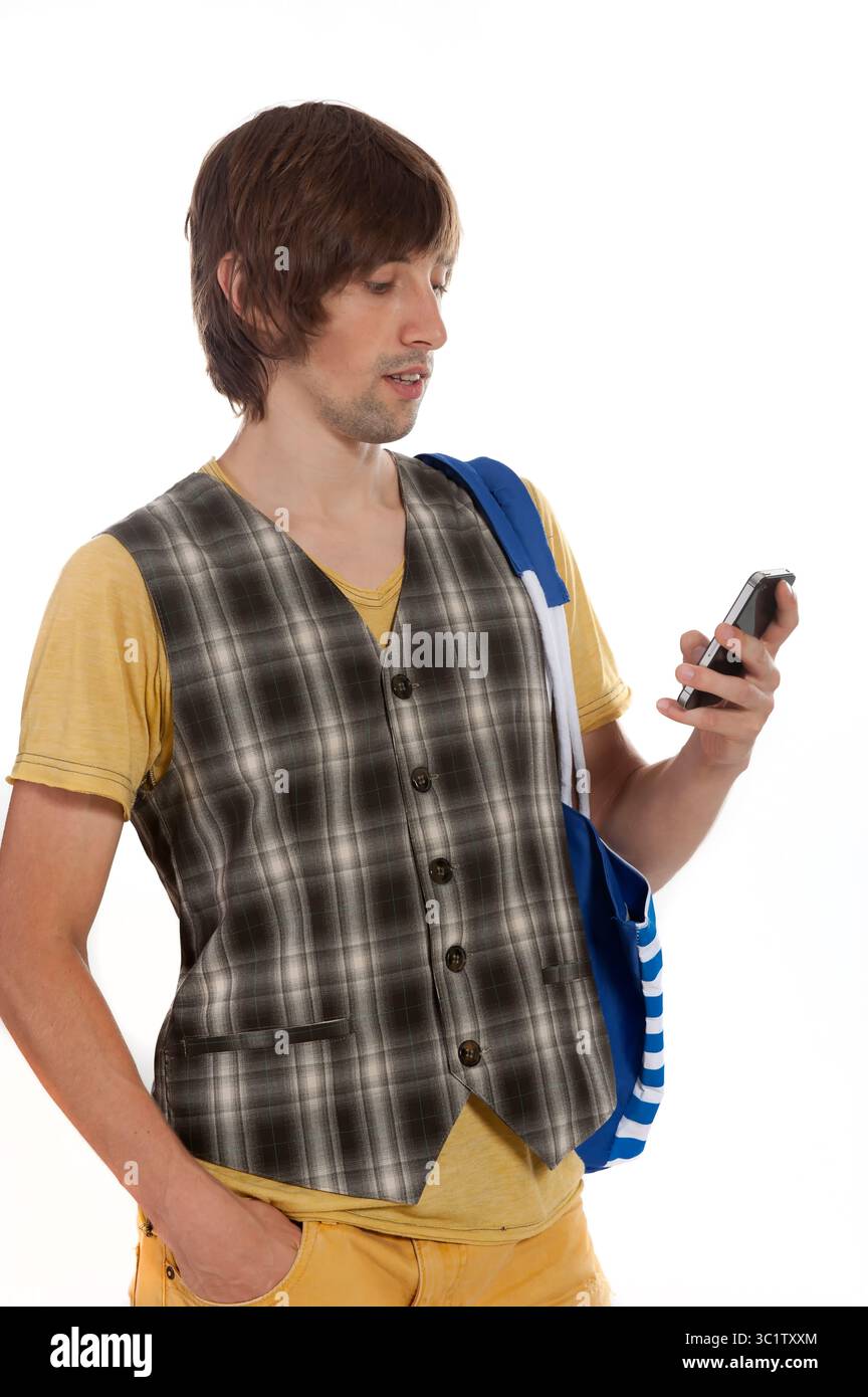 Ein junger Mann mit zotteligen Haaren schaut auf sein Smartphone, während er eine Weste trägt. Stockfoto
