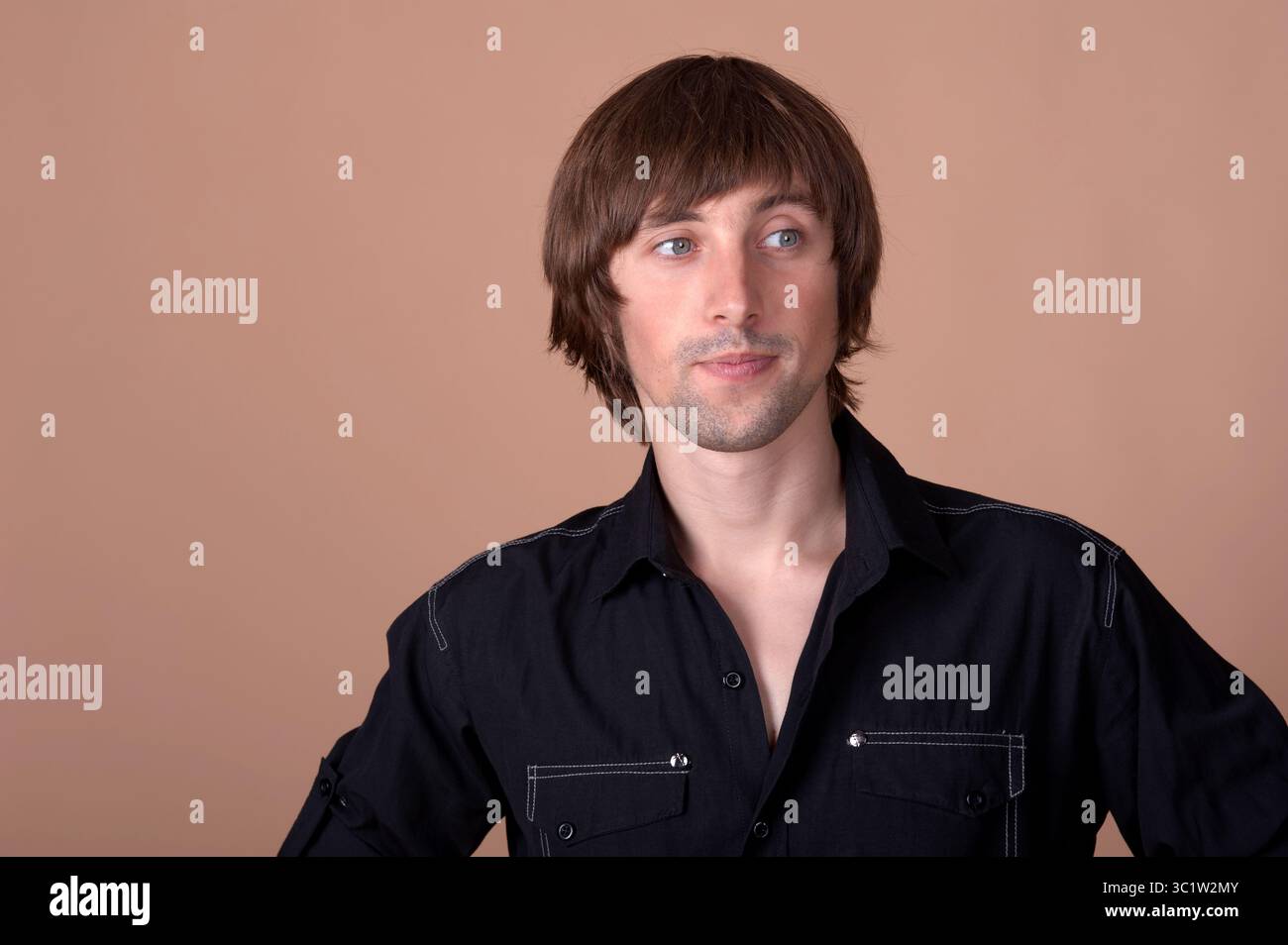 Ein Mann steht entspannt, trägt ein stylisches schwarzes Hemd und einen durchdachten Look. Stockfoto