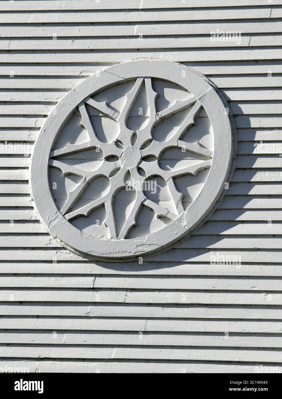 Ein weißer Holzkreis oder Rad ist an der United Church of Christ des Weißen Hauses in Waterbury, Vermont, montiert. Das Emblem ist rustikal und rau. Stockfoto