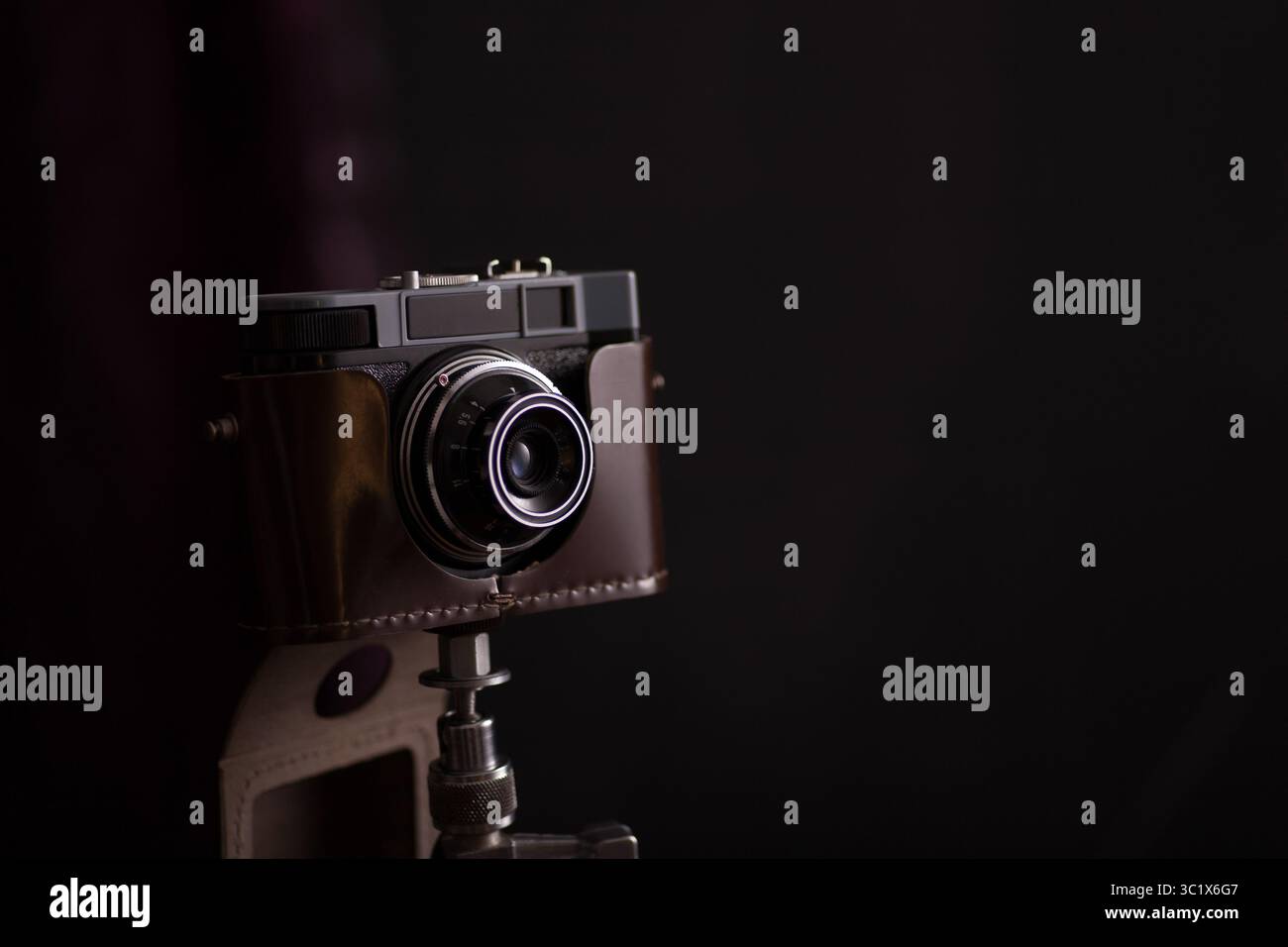 Eine Vintage-Kamera ist auf einem Stativ montiert und vor einem dunklen Hintergrund positioniert. Die Kamera ist in braunes Leder gewickelt und hat ein strukturiertes Objektiv. Stockfoto