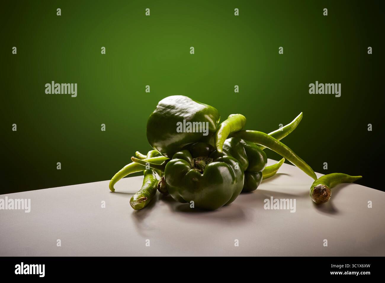 Eine Gruppe frischer grüner Paprika liegt auf einer weißen Oberfläche, die von einem sanften, grünen Licht beleuchtet wird. Die Paprika sind dicht gepackt und zeigen ihr V Stockfoto